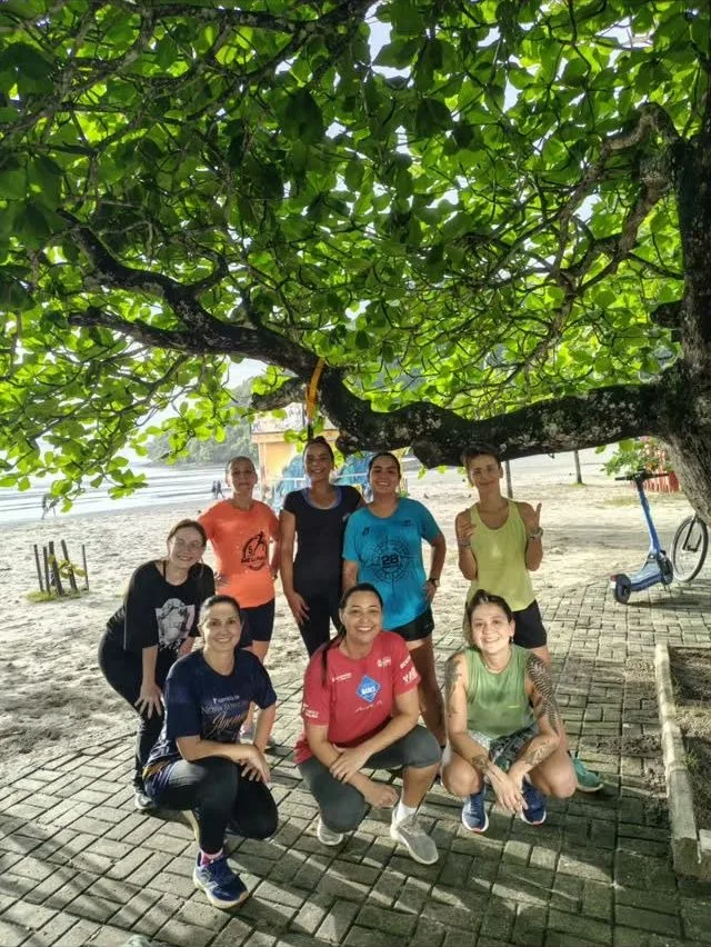 Grupo de alunos sob uma árvore, na orla, de manhã
